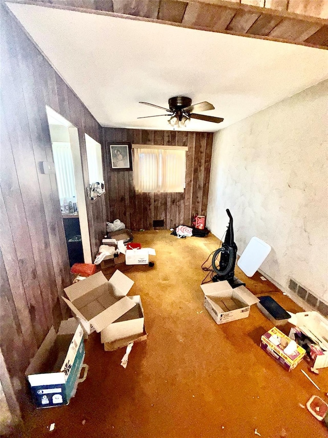 misc room with carpet, visible vents, wood walls, and a ceiling fan