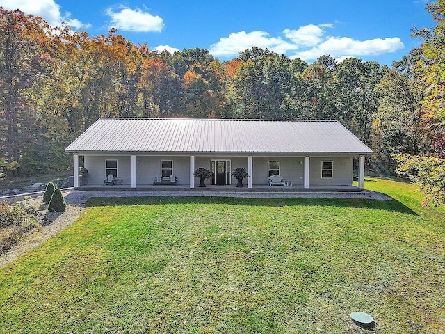 view of front facade featuring a wooded view, a front lawn, metal roof, and covered porch