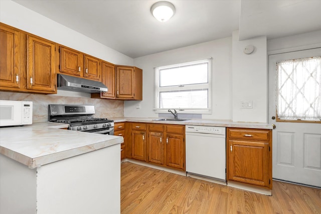 kitchen with light wood-type flooring, a sink, light countertops, under cabinet range hood, and white appliances
