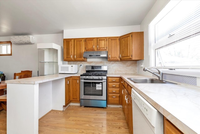 kitchen featuring a peninsula, white appliances, a wall mounted air conditioner, under cabinet range hood, and a sink