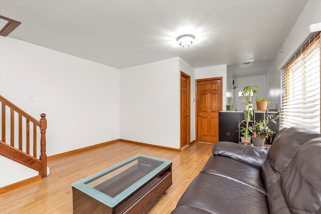 living area with baseboards, light wood-style flooring, and stairway