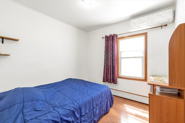 bedroom featuring crown molding, baseboard heating, and wood finished floors