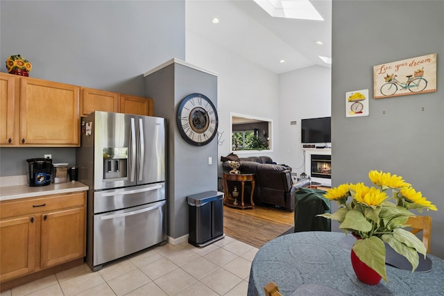 kitchen with light tile patterned flooring, light countertops, high vaulted ceiling, stainless steel refrigerator with ice dispenser, and a skylight