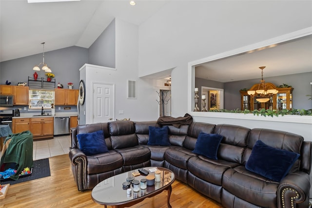 living area featuring light wood-type flooring, a notable chandelier, high vaulted ceiling, and visible vents