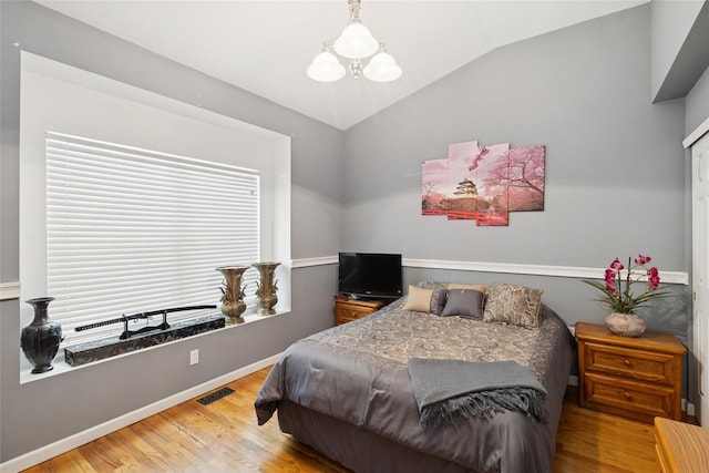 bedroom with visible vents, lofted ceiling, a notable chandelier, and wood finished floors