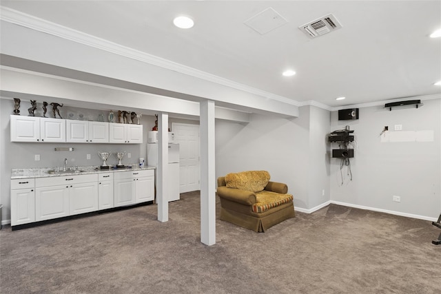 finished below grade area featuring visible vents, a sink, ornamental molding, and indoor wet bar