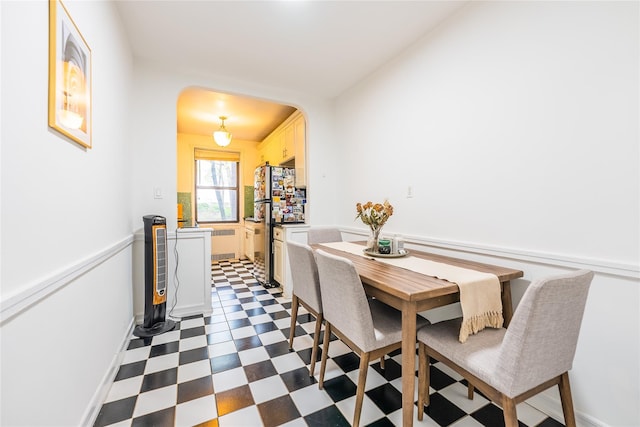 dining room featuring dark floors, arched walkways, baseboards, and radiator