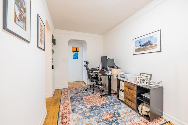 office area with crown molding, arched walkways, baseboards, and light wood-style flooring