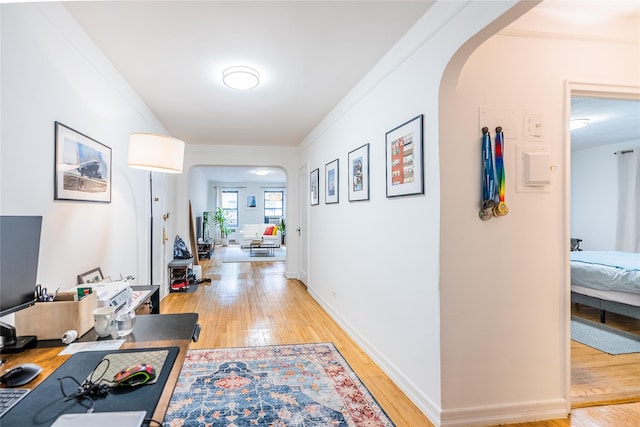 corridor featuring arched walkways, ornamental molding, and light wood-style flooring