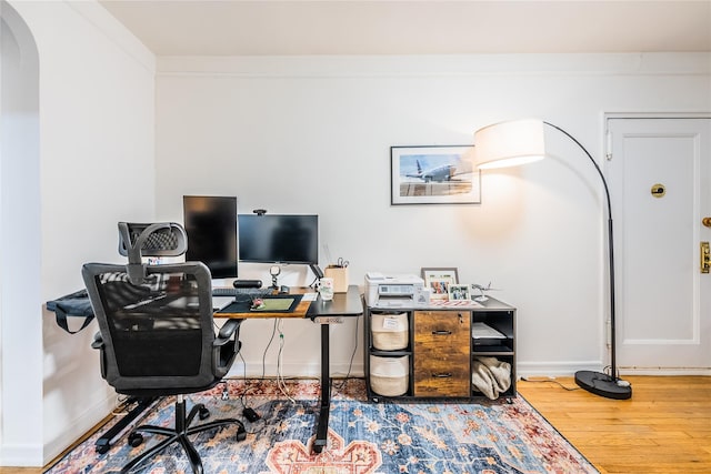 office area with arched walkways, baseboards, and wood finished floors