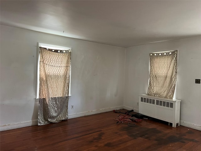 spare room featuring radiator heating unit, baseboards, and wood finished floors