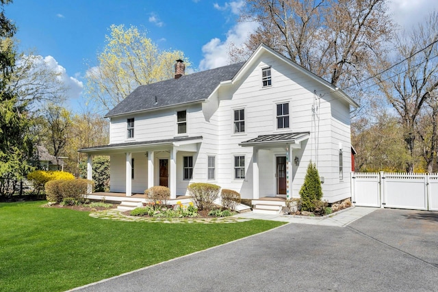 view of front of home with a front lawn, fence, covered porch, a chimney, and a gate