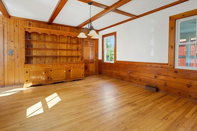 unfurnished room with beamed ceiling, light wood finished floors, wood walls, and a chandelier
