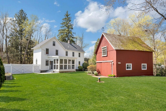 rear view of property featuring fence, a sunroom, a gate, an outbuilding, and a lawn