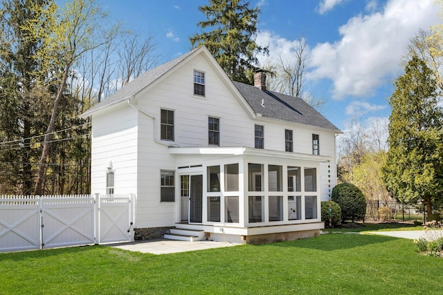 rear view of property featuring fence, a chimney, a sunroom, a gate, and a lawn