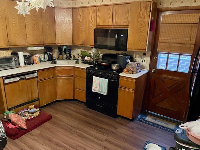 kitchen with black appliances, a sink, dark wood-type flooring, and light countertops