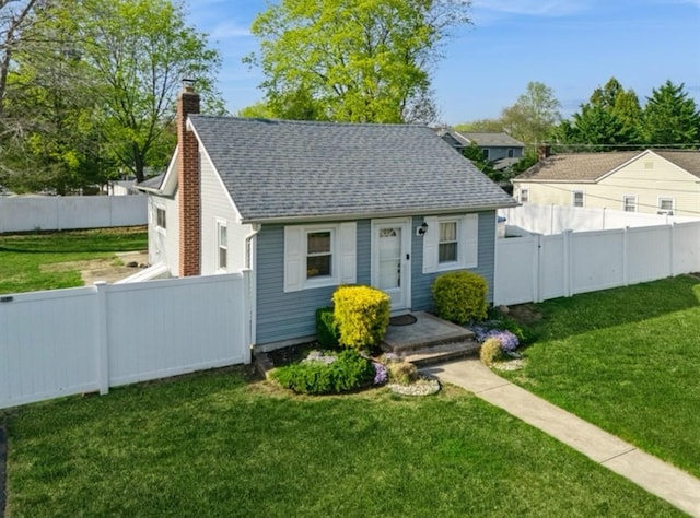 view of front facade featuring a chimney, a shingled roof, a front lawn, and a fenced backyard