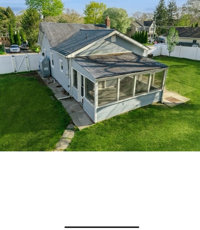 rear view of house with a fenced backyard, a gate, a sunroom, roof with shingles, and a lawn