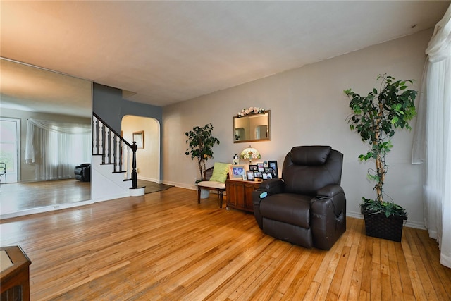sitting room with baseboards, arched walkways, stairway, and light wood-style floors