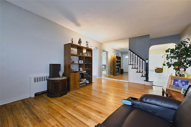 living room featuring radiator, arched walkways, hardwood / wood-style floors, and stairs