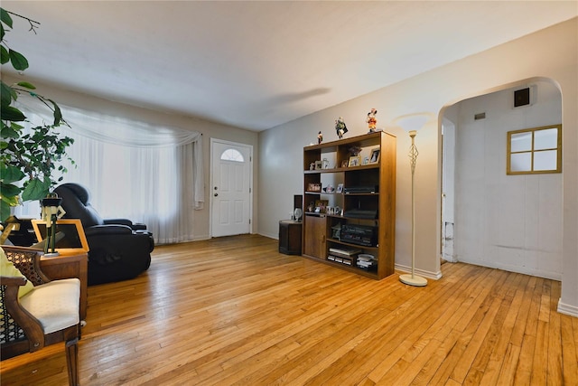 living room featuring baseboards, arched walkways, a wealth of natural light, and light wood finished floors