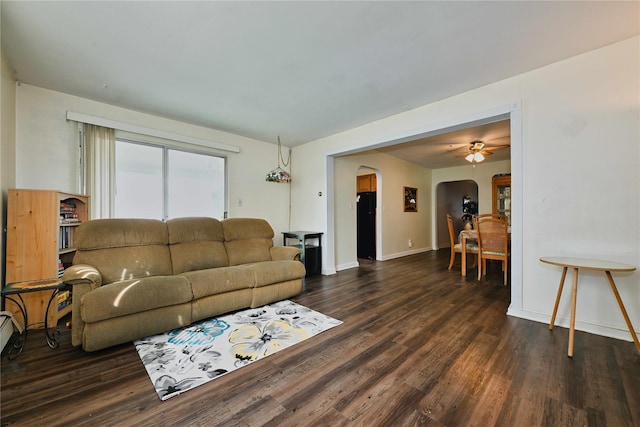 living area featuring arched walkways, ceiling fan, baseboards, and dark wood finished floors