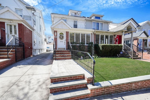 american foursquare style home featuring brick siding, entry steps, and a front yard