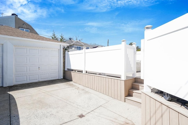 view of patio featuring a garage, concrete driveway, and fence