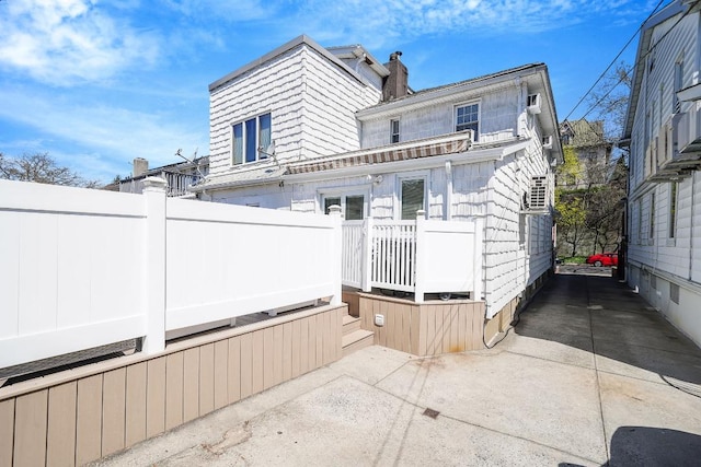 rear view of house featuring fence, a wooden deck, a chimney, and a patio area