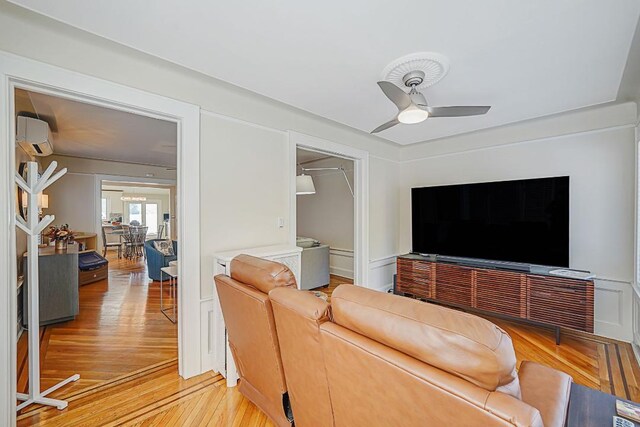 living room featuring light wood-style flooring, a wall unit AC, and ceiling fan