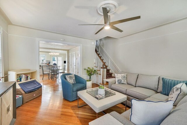 living room with light wood-type flooring, a ceiling fan, and stairs