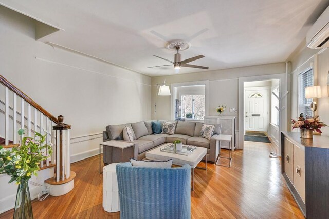 living area featuring stairway, ceiling fan, light wood-style flooring, and a wall unit AC