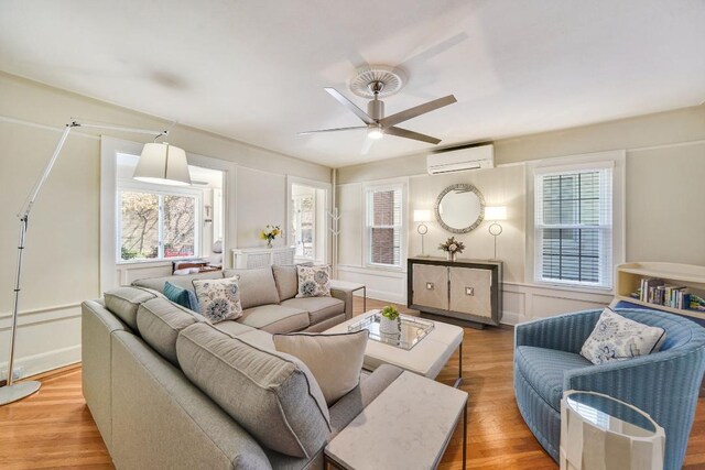 living area featuring wood finished floors, a decorative wall, wainscoting, a wall mounted AC, and ceiling fan