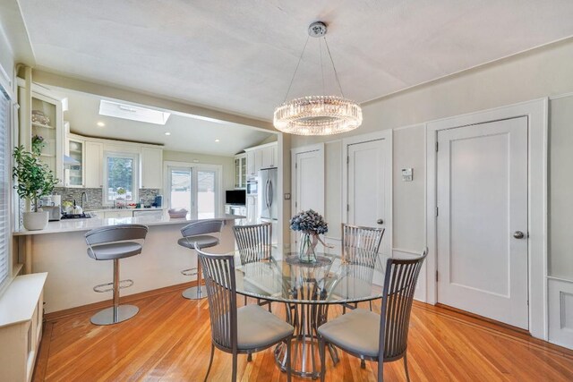 dining room with a chandelier, a skylight, and light wood-style flooring