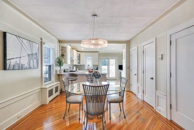 dining space featuring an inviting chandelier, radiator heating unit, light wood-style floors, and a decorative wall