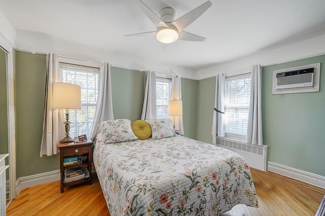 bedroom with baseboards, radiator heating unit, a wall mounted AC, and light wood-type flooring