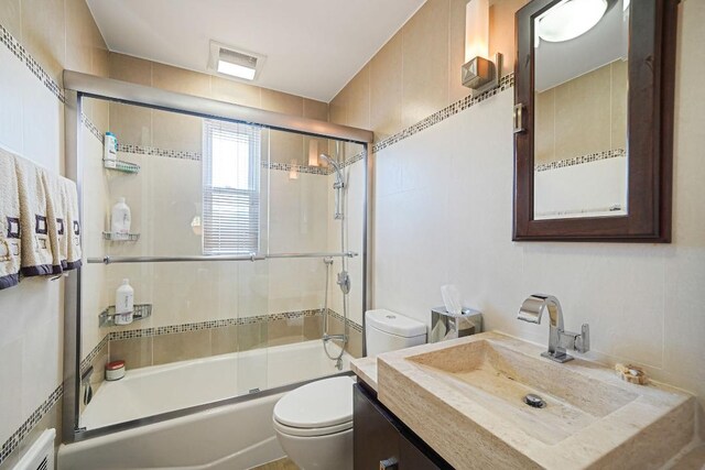 bathroom featuring vanity, visible vents, bath / shower combo with glass door, and toilet