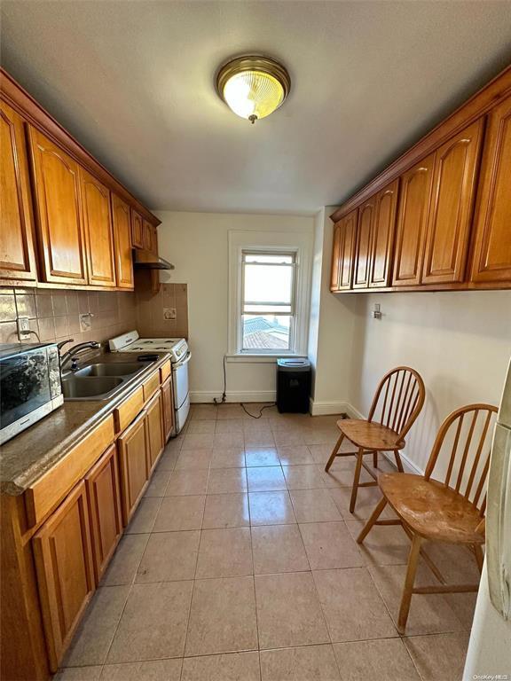 88-39 186th St, Hollis, NY 11423 - kitchen with stainless steel microwave, white range with electric cooktop, baseboards, and a sink
