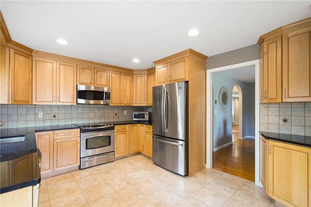 kitchen featuring arched walkways, dark countertops, backsplash, and appliances with stainless steel finishes