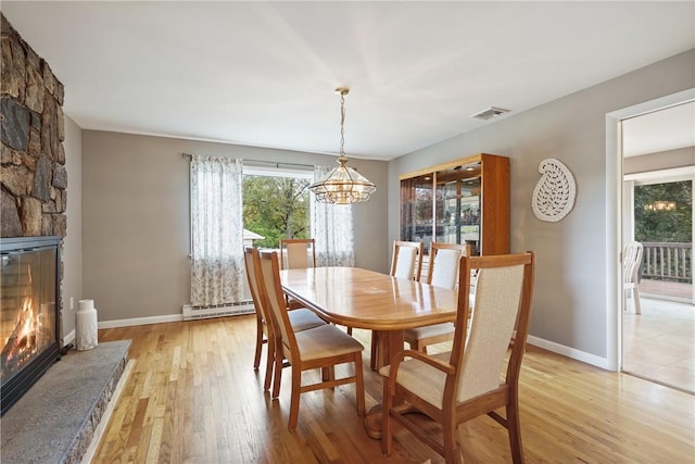 dining room with a baseboard radiator, a chandelier, light wood-style floors, a fireplace, and visible vents