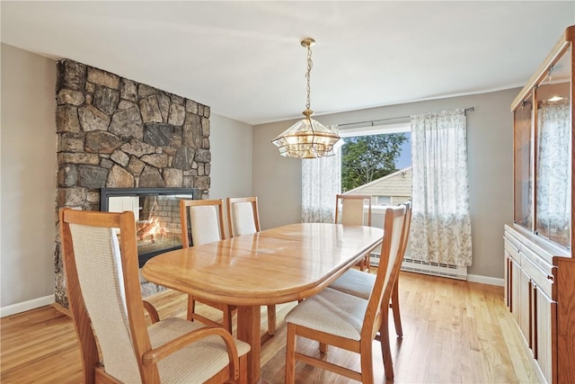 dining space featuring a stone fireplace, a baseboard heating unit, baseboards, light wood-style flooring, and a notable chandelier