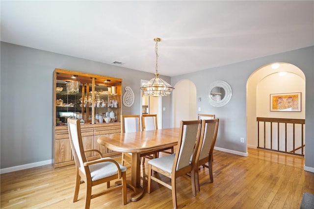 dining area with arched walkways, a chandelier, light wood-style flooring, and visible vents