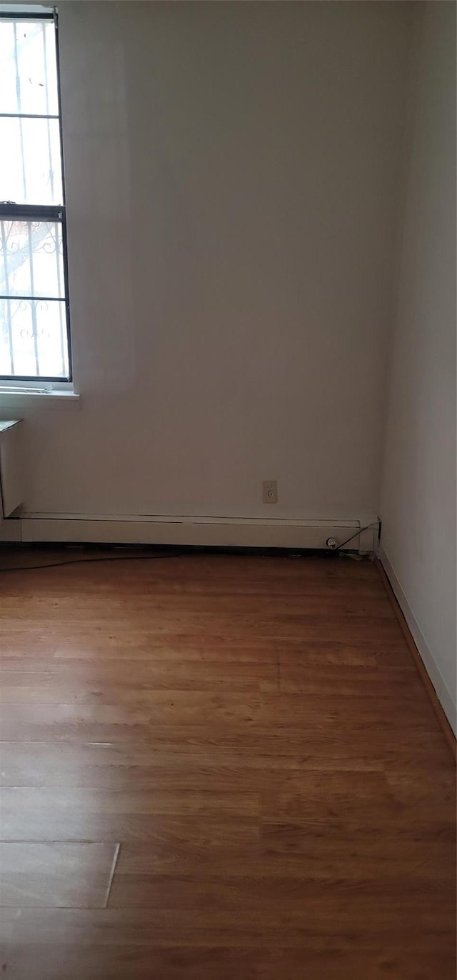 empty room featuring wood finished floors, baseboards, and a baseboard radiator