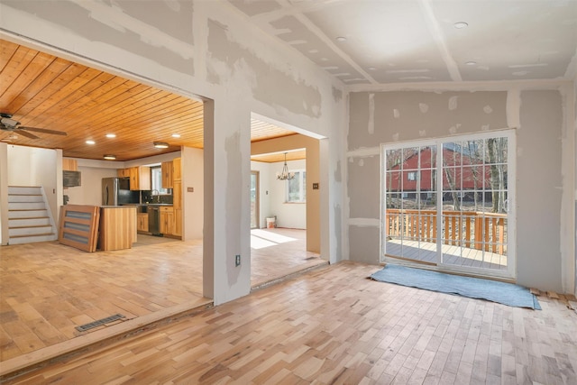 unfurnished living room featuring light wood finished floors, visible vents, a towering ceiling, and a healthy amount of sunlight