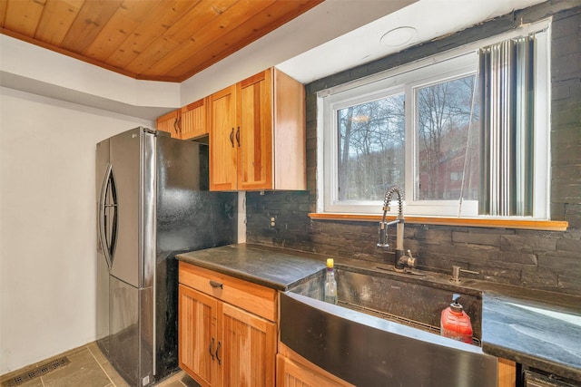 kitchen featuring dark countertops, wooden ceiling, a sink, freestanding refrigerator, and decorative backsplash
