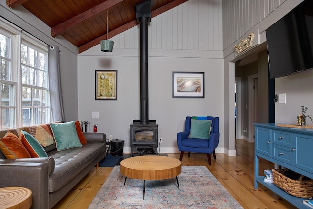 living room with wood ceiling, light wood-style flooring, beamed ceiling, a wood stove, and baseboards