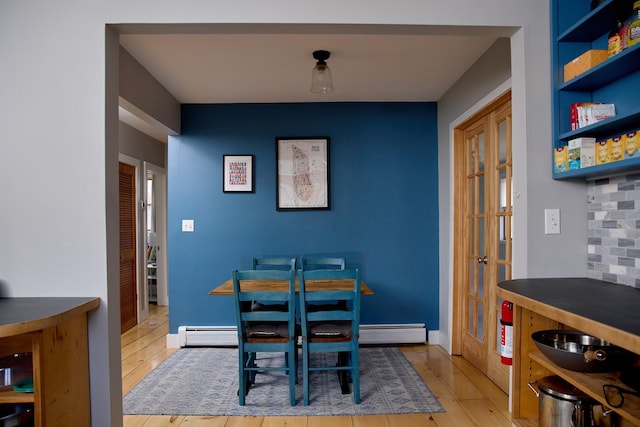 dining space featuring baseboard heating, baseboards, wood finished floors, and french doors