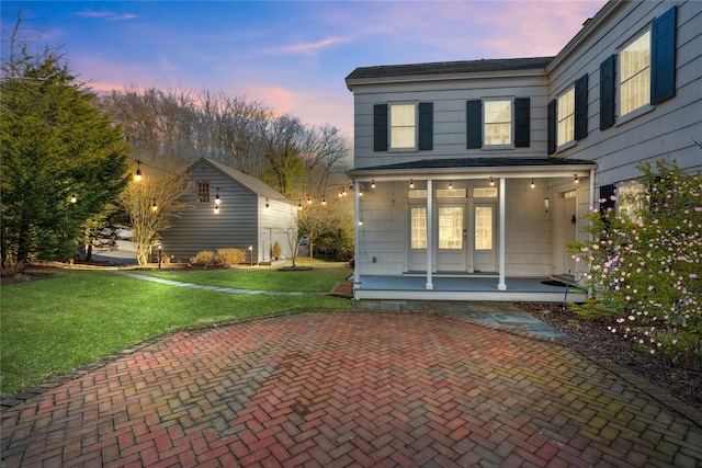 back of property at dusk with a yard, covered porch, and french doors