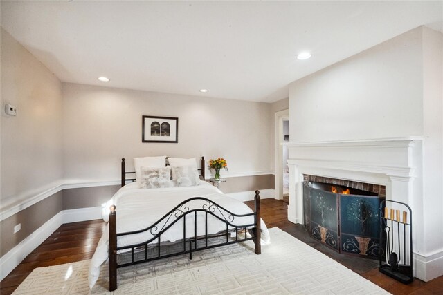bedroom featuring a fireplace with flush hearth, baseboards, wood finished floors, and recessed lighting