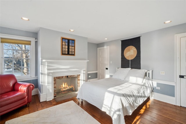 bedroom featuring hardwood / wood-style floors, baseboards, recessed lighting, and a warm lit fireplace